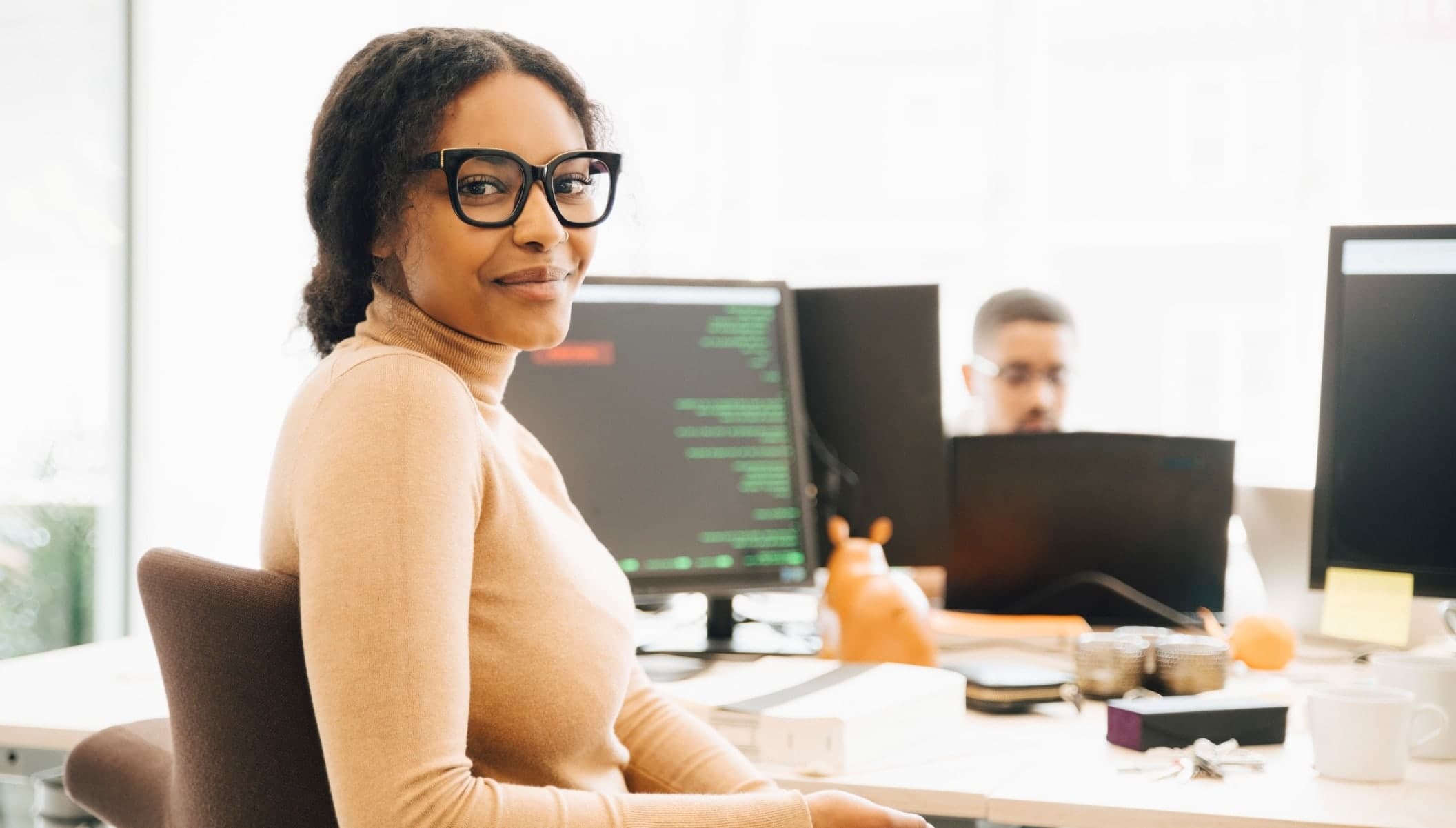 woman with glasses with computer screen behind her.