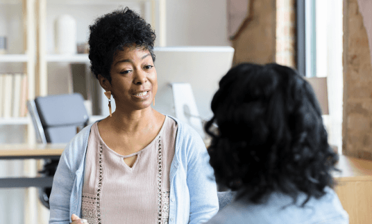 Two women having a conversation in an office setting.